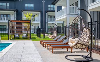 A modern outdoor pool area with a hanging chair and a pool table.